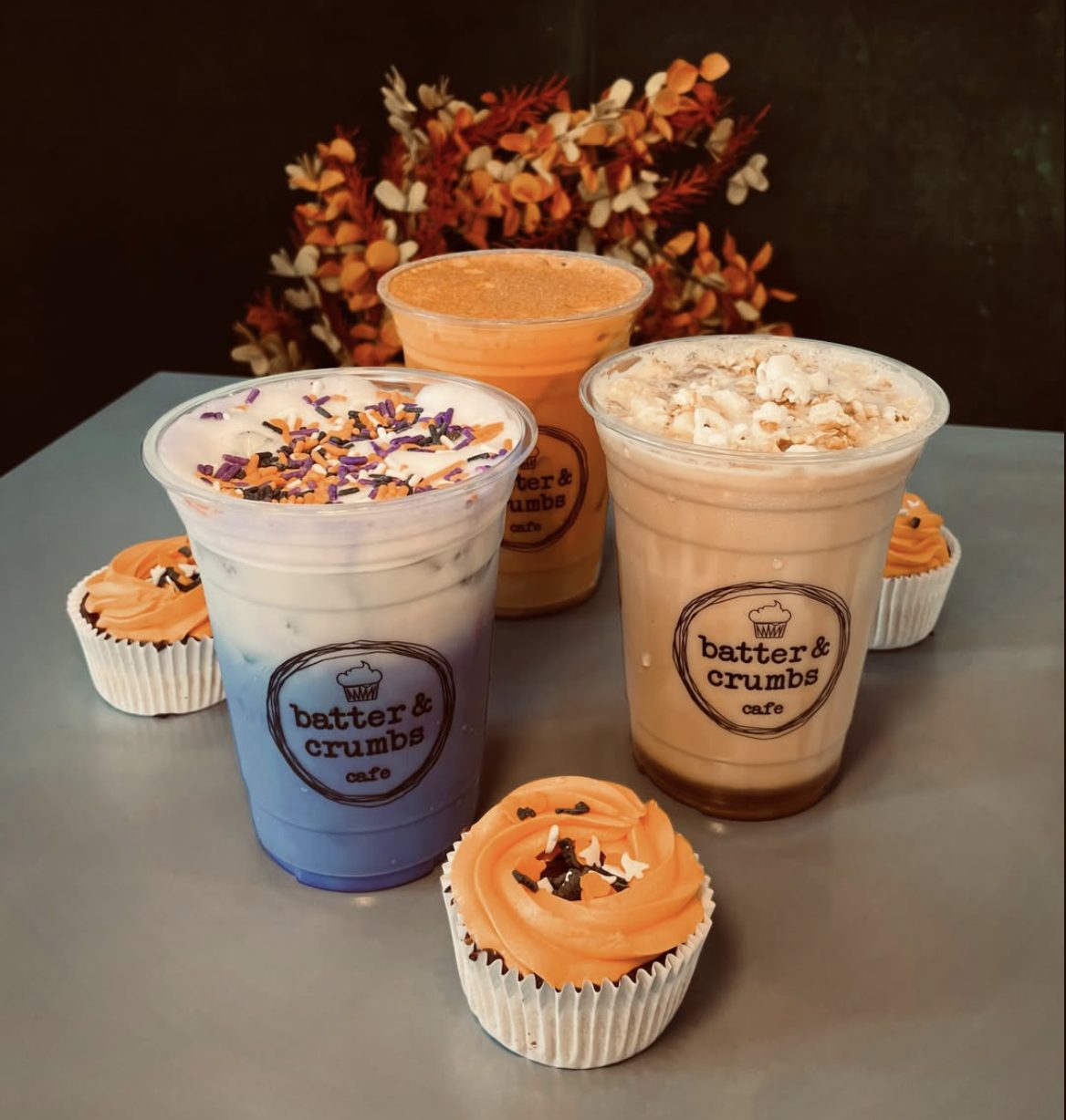 Three Batter & Crumbs fall drinks with Halloween cupcakes and fall leaves